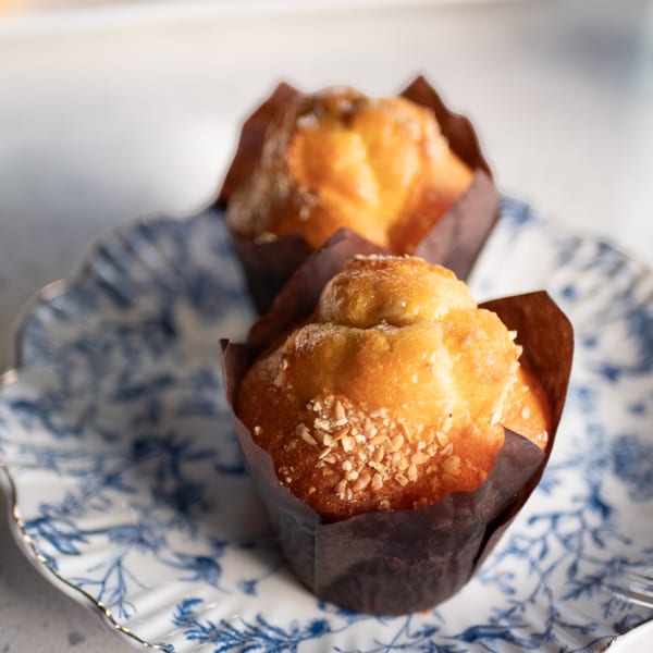 Two golden muffins with nuts on top, served in brown wrappers on a blue and white patterned plate.