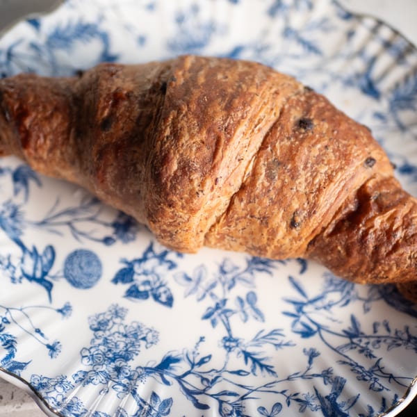A golden-brown chocolate croissant rests on a white plate with blue floral patterns.