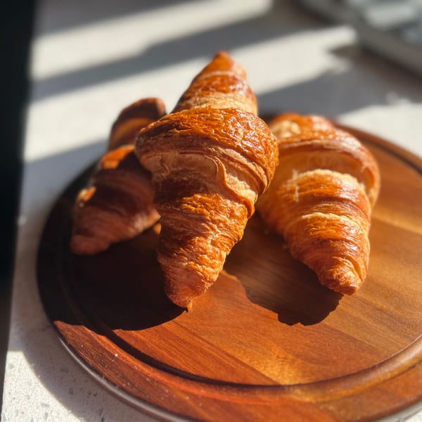 Golden-brown croissants on a wooden board, bathed in sunlight, at bean THERE cafe.