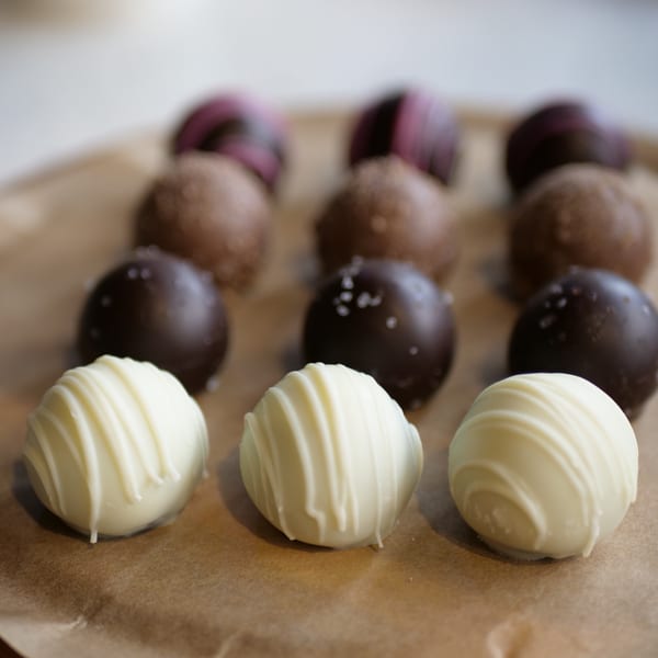 Rows of white chocolate, dark chocolate, and milk chocolate truffles on a brown paper surface.