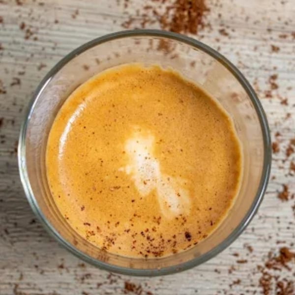 Overhead view of a glass of espresso with rich crema and scattered coffee grounds on a wooden surface.