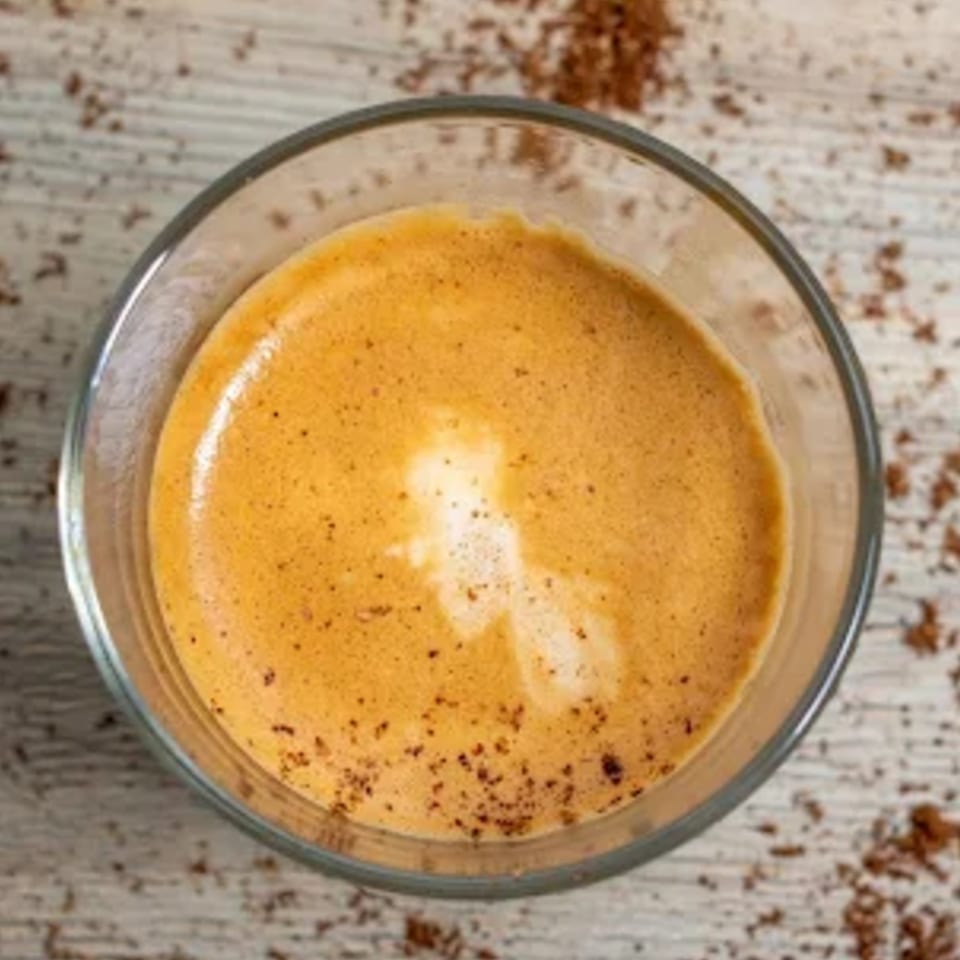 Overhead view of a glass of espresso with rich crema and scattered coffee grounds on a wooden surface.