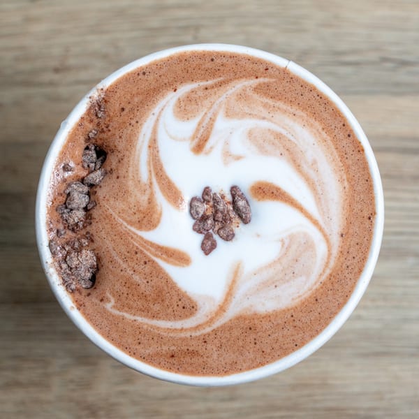 Overhead view of a hot chocolate with latte art and chocolate shavings in a white cup.